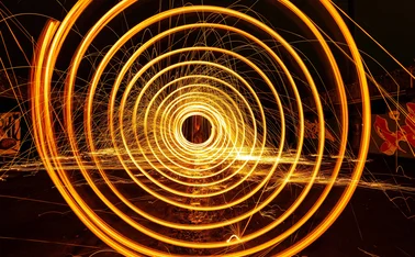 Long-exposure photograph of glowing orange light trails forming concentric circles and sparks, symbolising energy flow, data movement, or futuristic technology