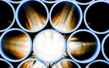 Close-up view of stacked industrial metal pipes with a glowing light source at the center, highlighting smooth circular interiors and polished steel surfaces
