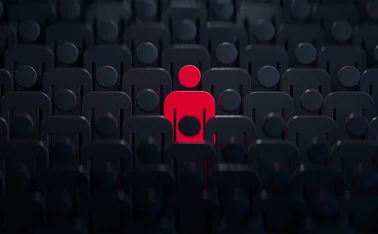 Stylised human outline coloured red, stood in the middle of many dark human outlines