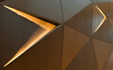 Abstract geometric wood wall with illuminated triangular openings and warm metallic textures