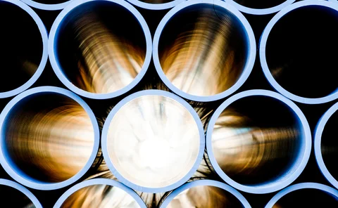 Close-up view of stacked industrial metal pipes with a glowing light source at the center, highlighting smooth circular interiors and polished steel surfaces