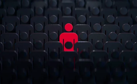Stylised human outline coloured red, stood in the middle of many dark human outlines