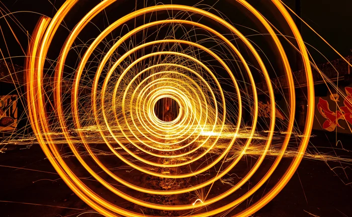 Long-exposure photograph of glowing orange light trails forming concentric circles and sparks, symbolising energy flow, data movement, or futuristic technology
