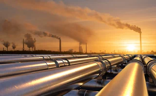 Pipelines leading to an oil refinery in golden sunset with chimneys in the background