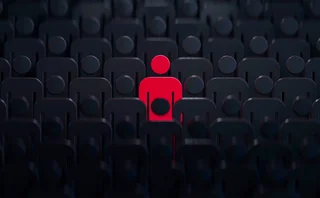 Stylised human outline coloured red, stood in the middle of many dark human outlines