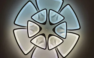 Modern LED light graphic featuring a dramatic geometric floral design. The fixture is composed of multiple tiers of illuminated triangles with black borders, creating a stylized flower pattern against a dark background.