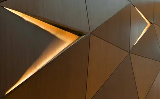 Abstract geometric wood wall with illuminated triangular openings and warm metallic textures