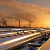 Pipelines leading to an oil refinery in golden sunset with chimneys in the background