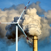 Wind turbine with a smoking chimney behind it 